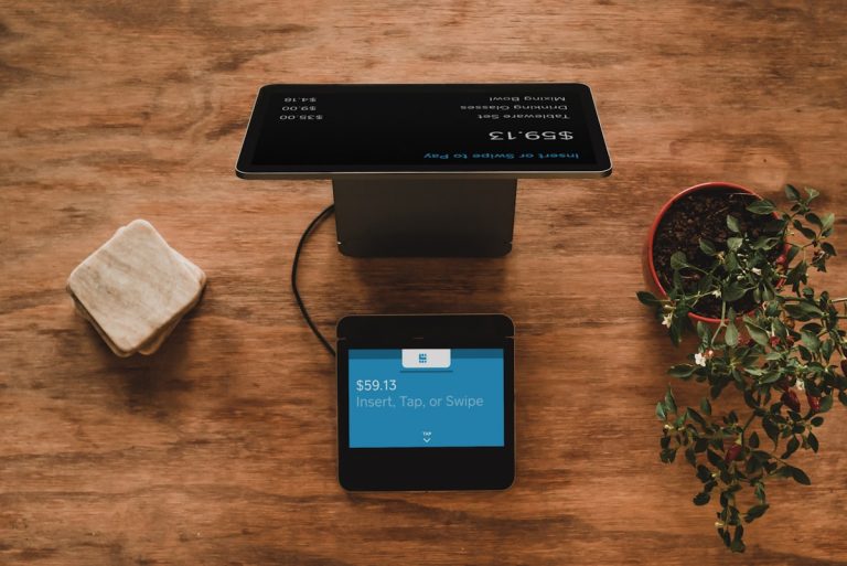 Payment terminal on a wooden table with a card reader displaying $59.13 and 'Insert, Tap, or Swipe' instructions.