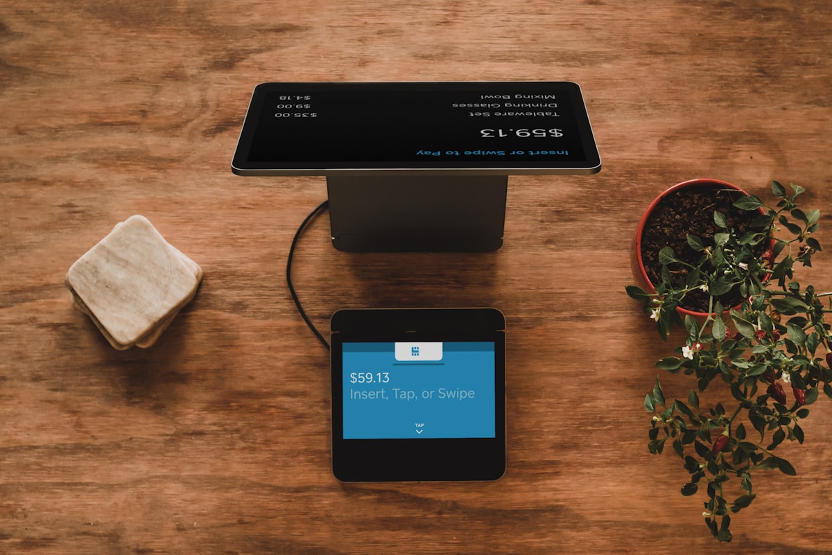 Payment terminal on a wooden table with a card reader displaying $59.13 and 'Insert, Tap, or Swipe' instructions.